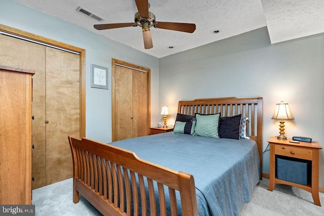 carpeted bedroom with multiple closets, ceiling fan, and a textured ceiling