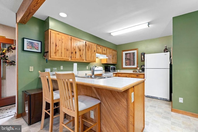 kitchen featuring range, white refrigerator, sink, kitchen peninsula, and a breakfast bar area