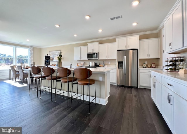 kitchen featuring dark hardwood / wood-style flooring, appliances with stainless steel finishes, a kitchen island with sink, white cabinets, and ornamental molding