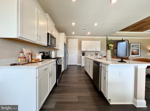 kitchen with dark wood-type flooring, a center island with sink, ornamental molding, appliances with stainless steel finishes, and white cabinetry