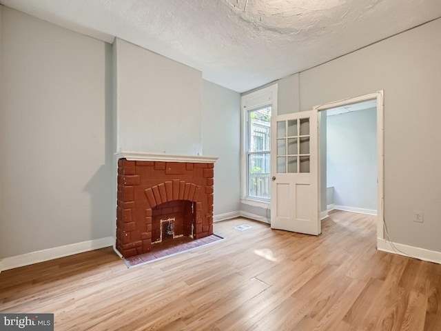 unfurnished living room featuring light hardwood / wood-style floors, a textured ceiling, and a brick fireplace