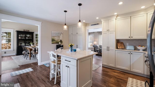 kitchen featuring pendant lighting, a kitchen island, dark wood-type flooring, white cabinetry, and tasteful backsplash