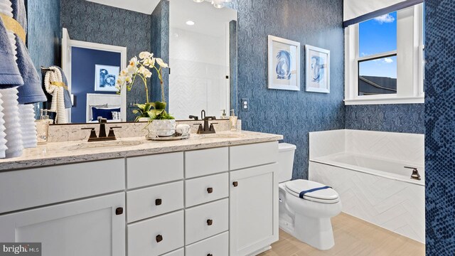 bathroom with tiled tub, vanity, and toilet