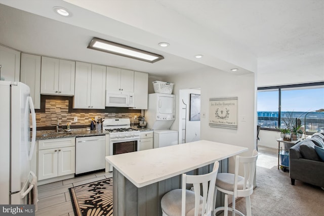 kitchen with a kitchen bar, stacked washing maching and dryer, white appliances, sink, and white cabinetry