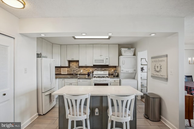 kitchen with white cabinetry, a kitchen breakfast bar, tasteful backsplash, white appliances, and stacked washer and clothes dryer