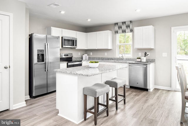 kitchen with a center island, appliances with stainless steel finishes, a kitchen bar, white cabinets, and light wood-type flooring