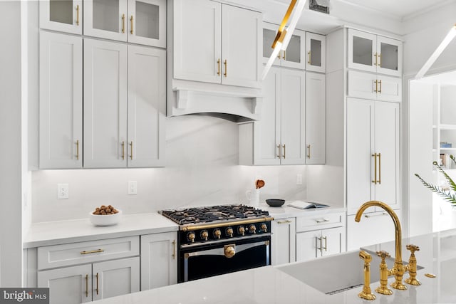 kitchen featuring white cabinetry, sink, high end range, and custom range hood