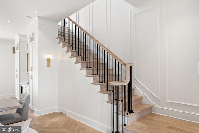 staircase with crown molding and parquet flooring