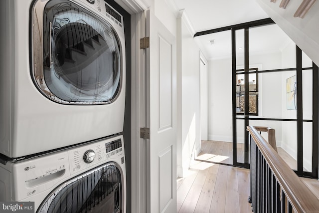 clothes washing area with crown molding, light hardwood / wood-style floors, and stacked washing maching and dryer