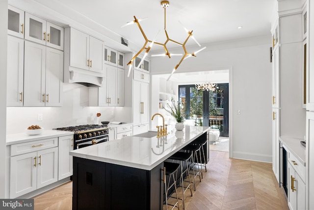 kitchen with white cabinetry, a chandelier, a kitchen island with sink, and light parquet floors