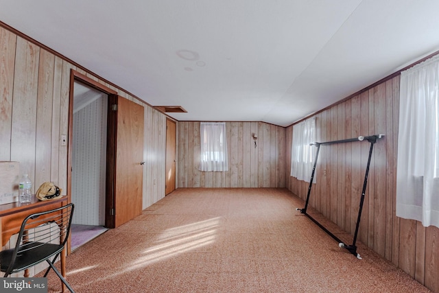 carpeted spare room with wooden walls, plenty of natural light, and vaulted ceiling