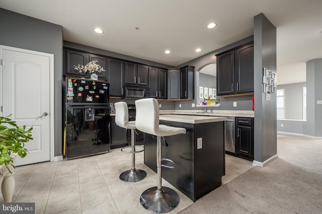 kitchen with black appliances, a center island, light colored carpet, and a breakfast bar area