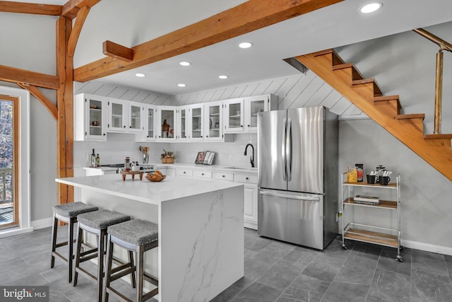 kitchen featuring a breakfast bar, sink, stainless steel fridge, a kitchen island, and white cabinetry