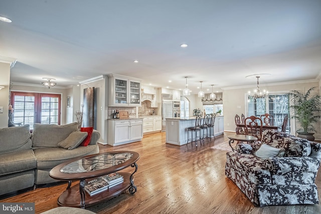 living room with french doors, light hardwood / wood-style flooring, a notable chandelier, and crown molding