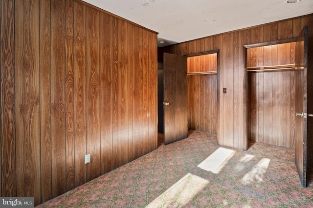 unfurnished bedroom featuring multiple closets, carpet, and wooden walls