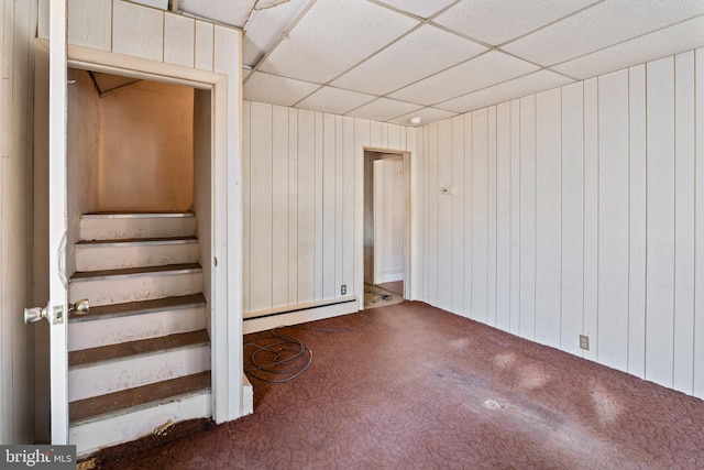 basement with a baseboard radiator, carpet, wood walls, and a paneled ceiling