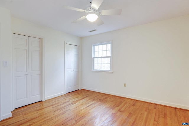 unfurnished bedroom with light hardwood / wood-style flooring, ceiling fan, and multiple closets