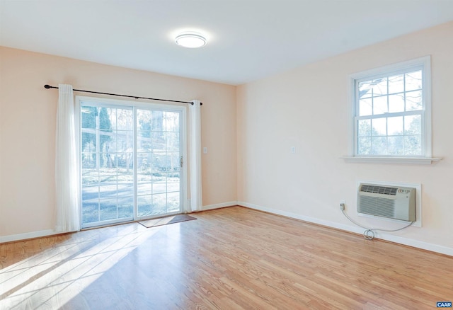 spare room with a wall mounted air conditioner, a healthy amount of sunlight, and light hardwood / wood-style flooring