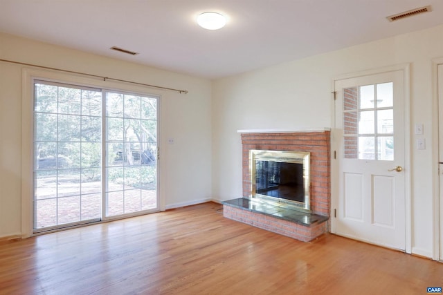 unfurnished living room featuring wood-type flooring and a brick fireplace