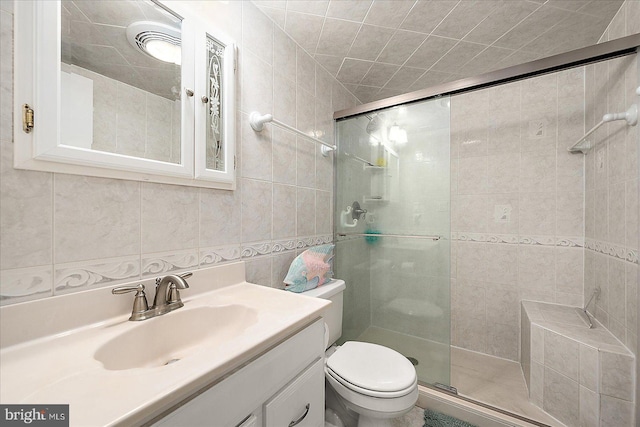 bathroom featuring vanity, a shower with door, toilet, and tile walls