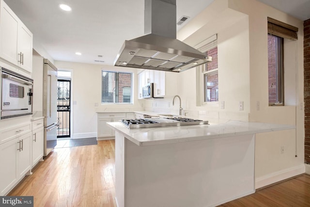 kitchen with kitchen peninsula, white cabinetry, white microwave, and island exhaust hood