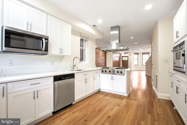 kitchen featuring light wood-type flooring, island range hood, stainless steel appliances, sink, and white cabinets