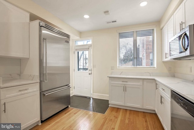 kitchen with light hardwood / wood-style floors, light stone countertops, white cabinetry, and appliances with stainless steel finishes