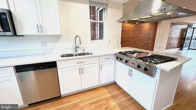 kitchen with appliances with stainless steel finishes, light hardwood / wood-style floors, extractor fan, and brick wall