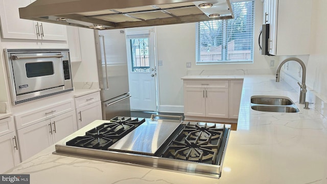 kitchen with light stone counters, stainless steel appliances, sink, exhaust hood, and white cabinetry