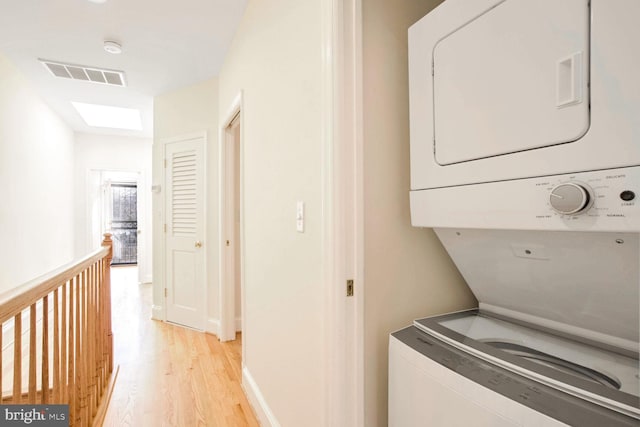 washroom with a skylight, stacked washer and dryer, and light wood-type flooring