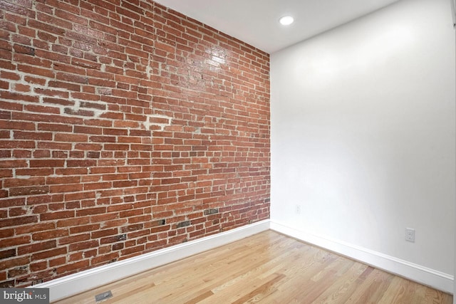 empty room featuring brick wall and hardwood / wood-style flooring