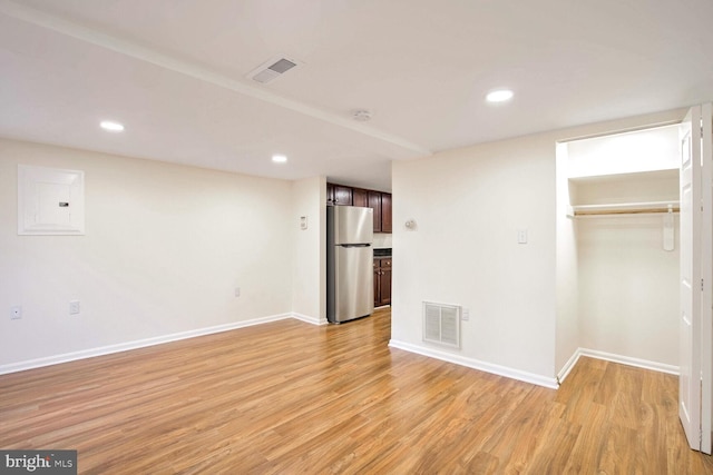 unfurnished bedroom featuring electric panel, light hardwood / wood-style flooring, stainless steel refrigerator, and a closet