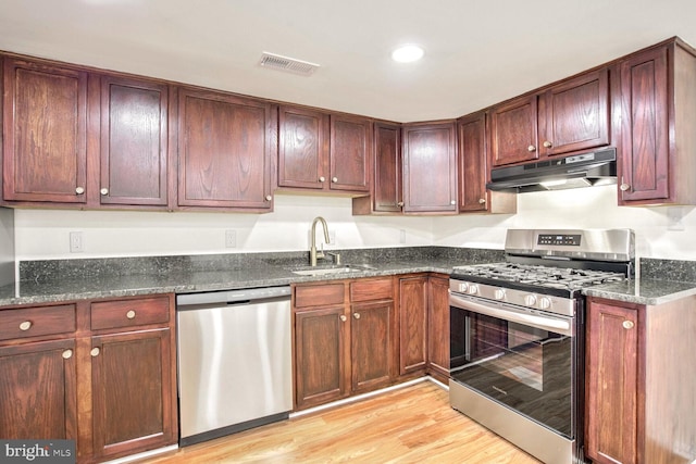 kitchen with appliances with stainless steel finishes, sink, light hardwood / wood-style flooring, and dark stone countertops