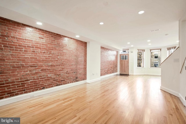 unfurnished living room featuring brick wall and light hardwood / wood-style floors