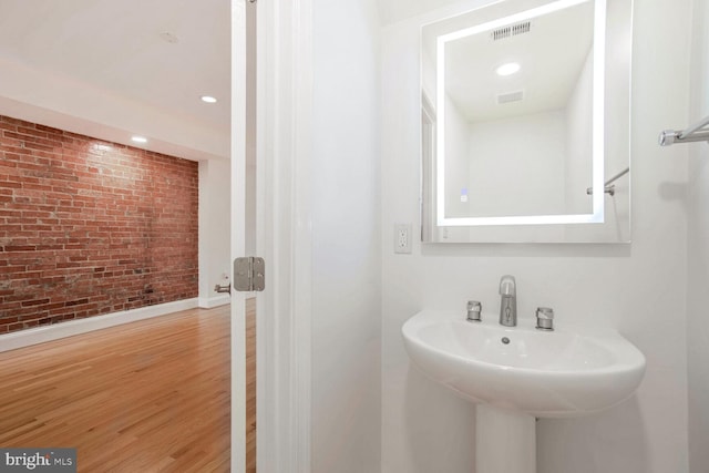 bathroom featuring wood-type flooring and brick wall