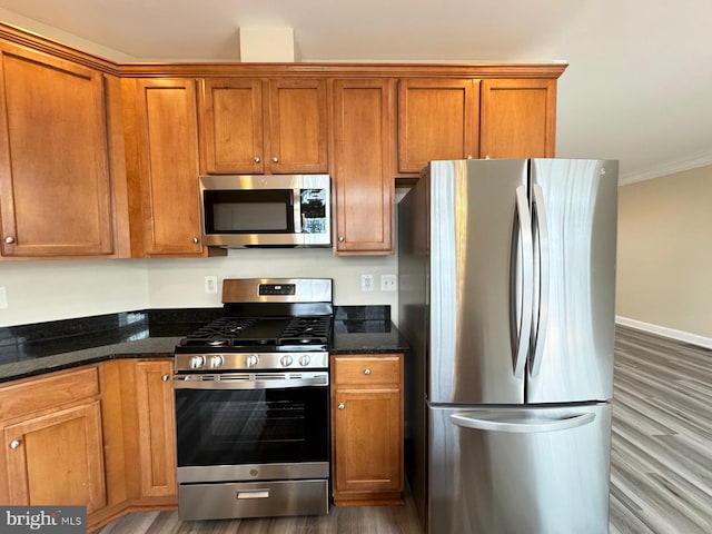 kitchen with dark stone counters, crown molding, stainless steel appliances, and wood-type flooring