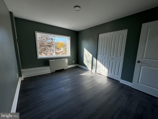 unfurnished bedroom with radiator, a closet, and dark wood-type flooring