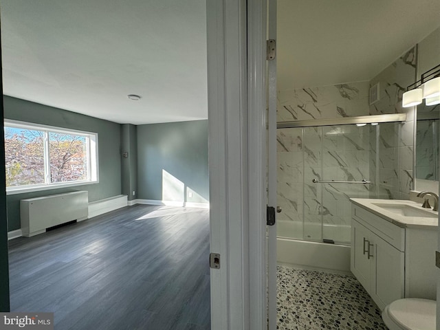 full bathroom with vanity, shower / bath combination with glass door, radiator heating unit, toilet, and wood-type flooring