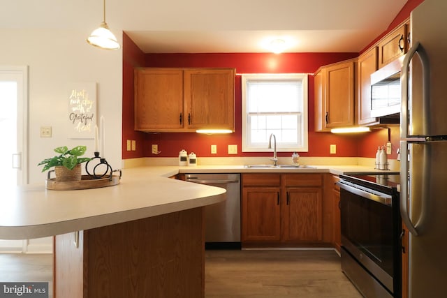 kitchen featuring sink, kitchen peninsula, decorative light fixtures, appliances with stainless steel finishes, and hardwood / wood-style flooring