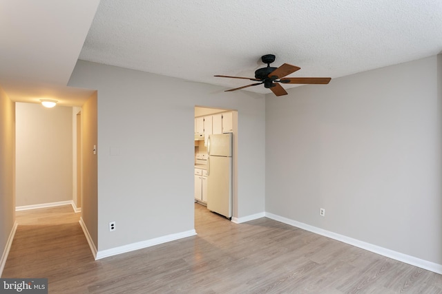 unfurnished bedroom with a textured ceiling, light hardwood / wood-style flooring, white fridge, ensuite bathroom, and ceiling fan