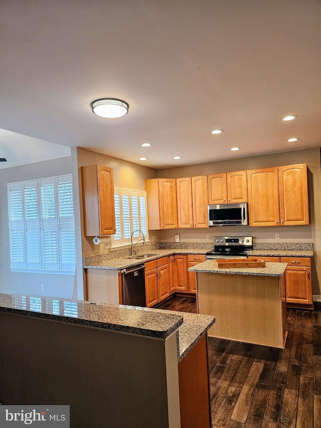 kitchen featuring sink, a center island, stainless steel appliances, light stone countertops, and dark wood-type flooring