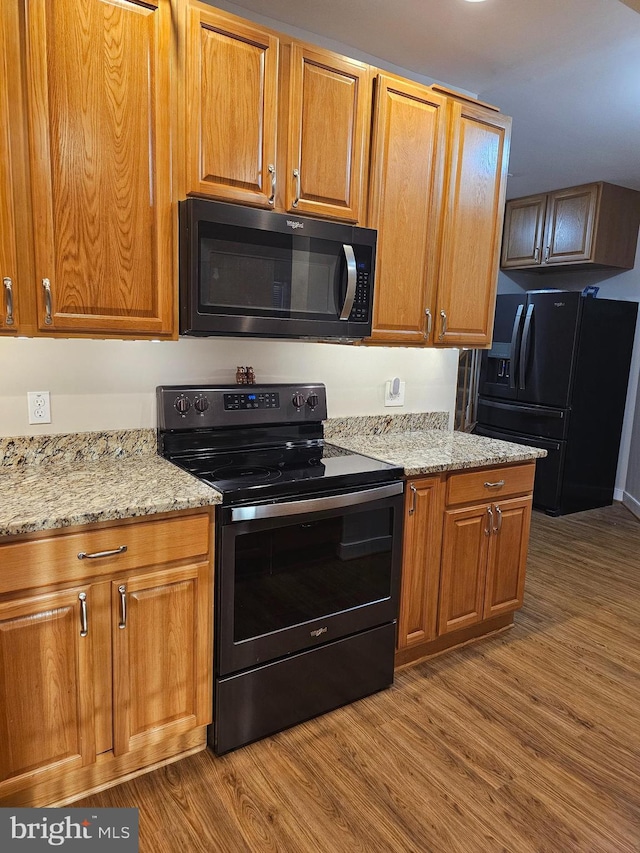 kitchen featuring light stone countertops, hardwood / wood-style flooring, and black appliances