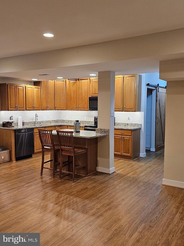 kitchen featuring a breakfast bar area, a barn door, a center island, black appliances, and light stone countertops