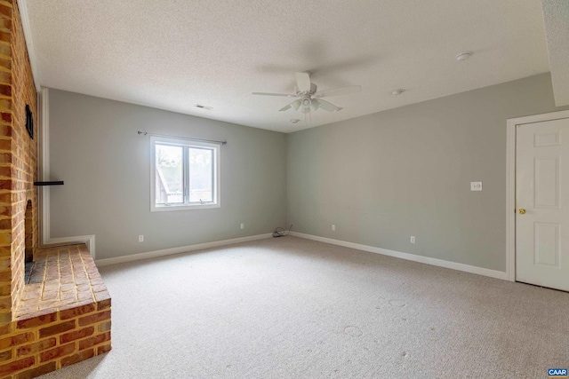 unfurnished living room featuring ceiling fan, carpet floors, a textured ceiling, and a brick fireplace