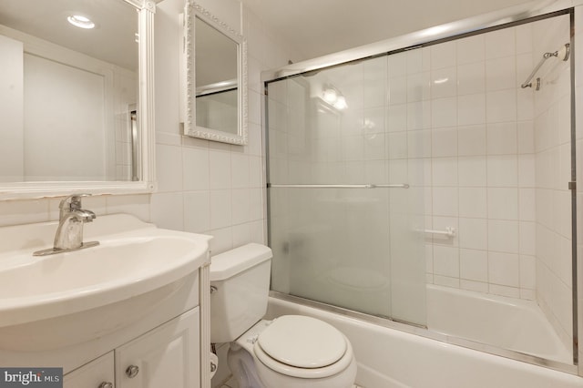 full bathroom featuring combined bath / shower with glass door, vanity, toilet, and tile walls