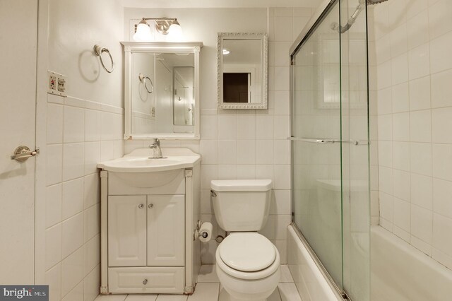 full bathroom featuring tile patterned flooring, toilet, shower / bath combination with glass door, vanity, and tile walls