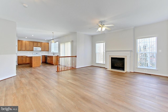 unfurnished living room featuring ceiling fan with notable chandelier and light hardwood / wood-style flooring