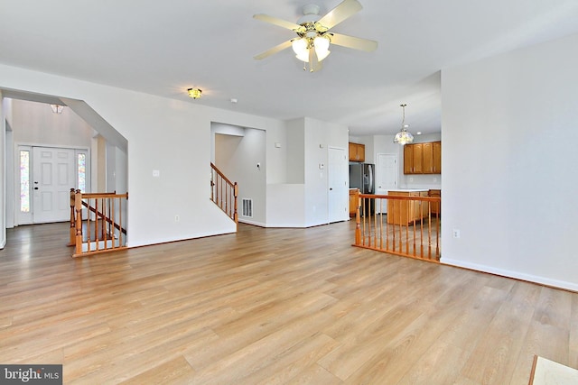 unfurnished living room with ceiling fan with notable chandelier and light wood-type flooring