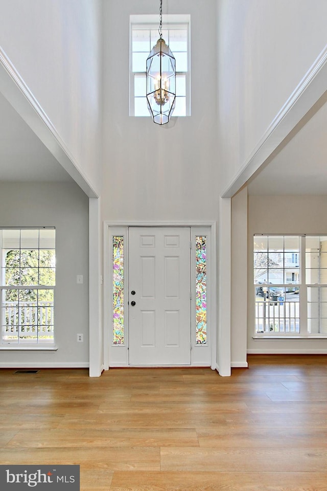 entrance foyer with light hardwood / wood-style flooring, a towering ceiling, a healthy amount of sunlight, and an inviting chandelier