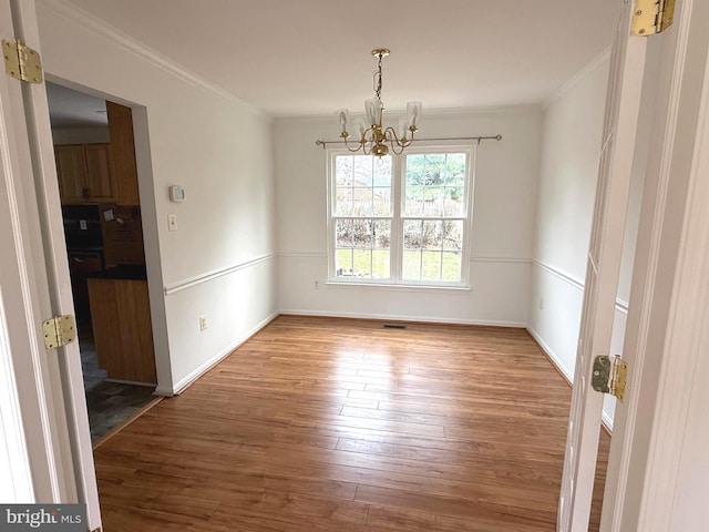 unfurnished dining area featuring a chandelier, wood-type flooring, and crown molding